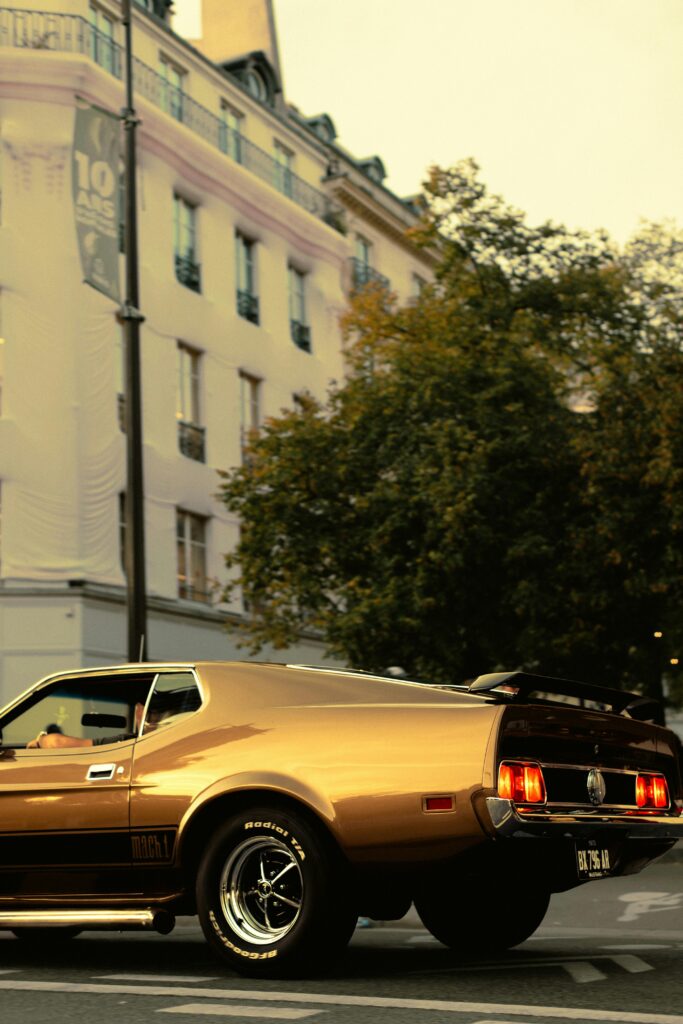Classic golden Mustang parked on an urban street corner at dusk.