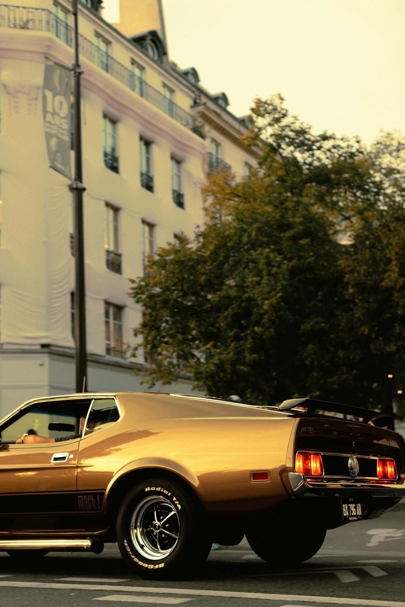 Classic golden Mustang parked on an urban street corner at dusk.